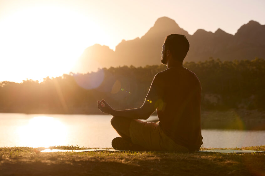 man meditating in front of a lake surrounded by mountains at sunrise